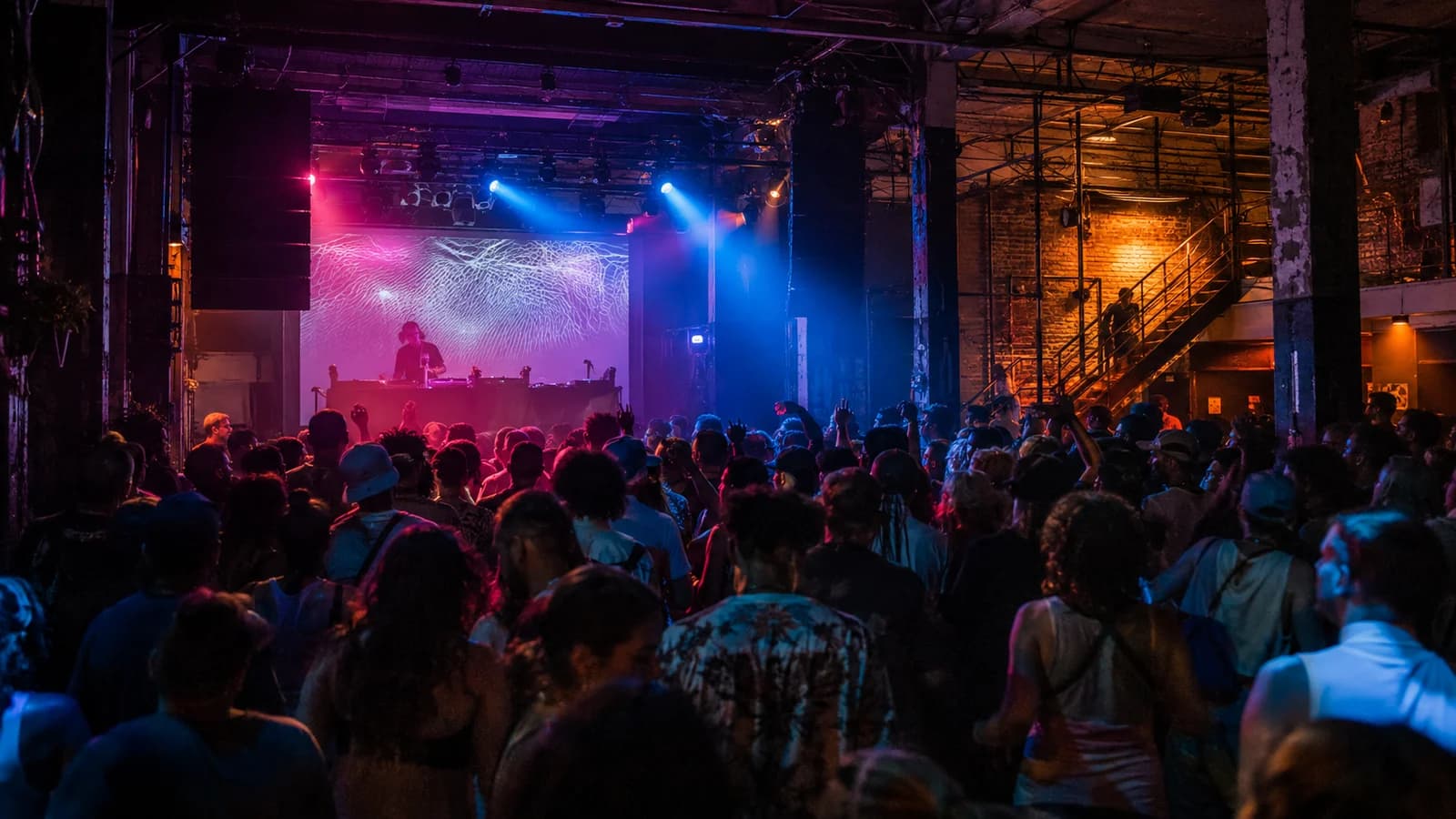 Crowd dancing under cobalt and magenta lights in an industrial multi-room Bushwick music venue