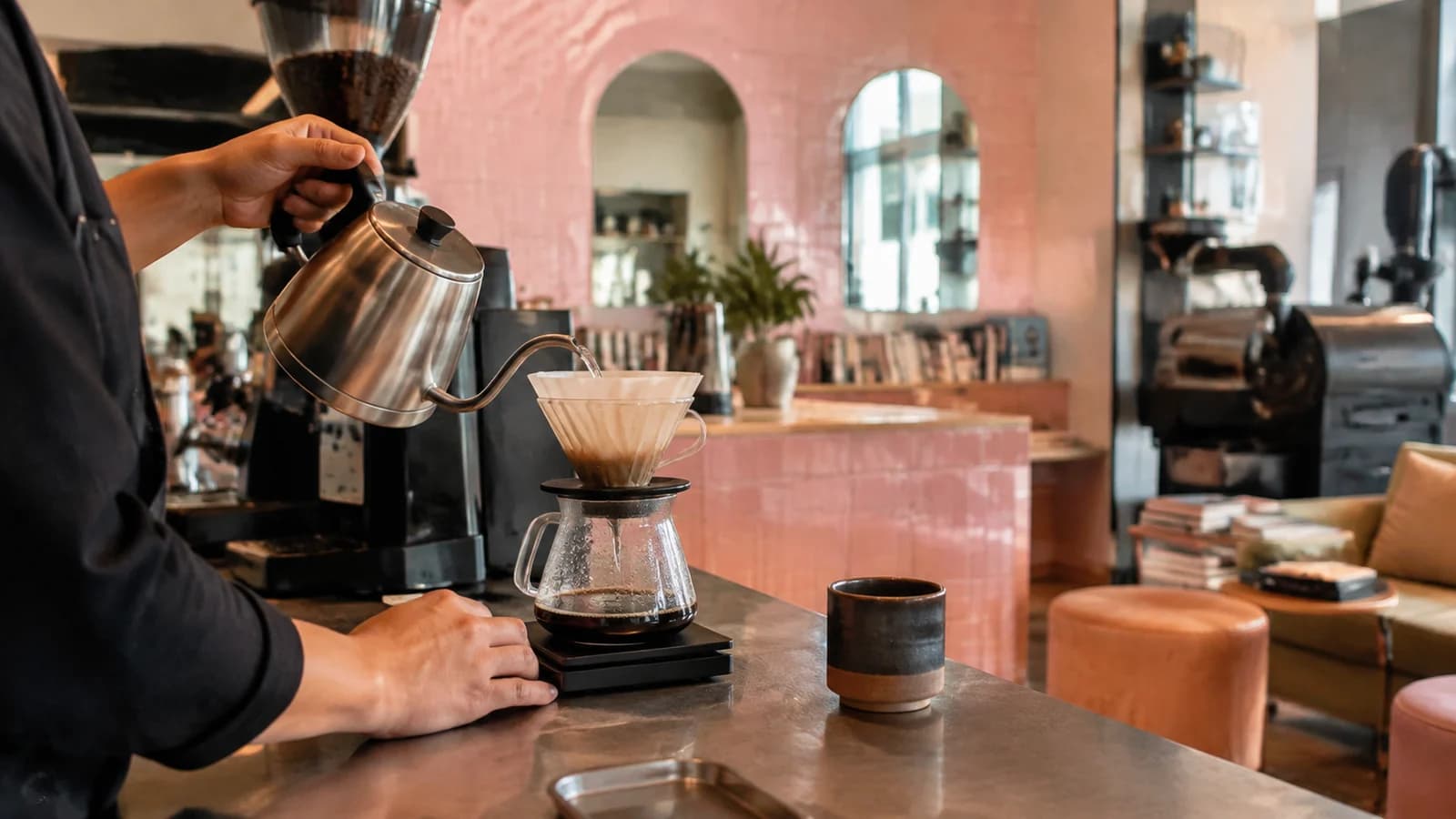 Barista preparing pour-over coffee at a pink-tiled independent Bushwick cafe